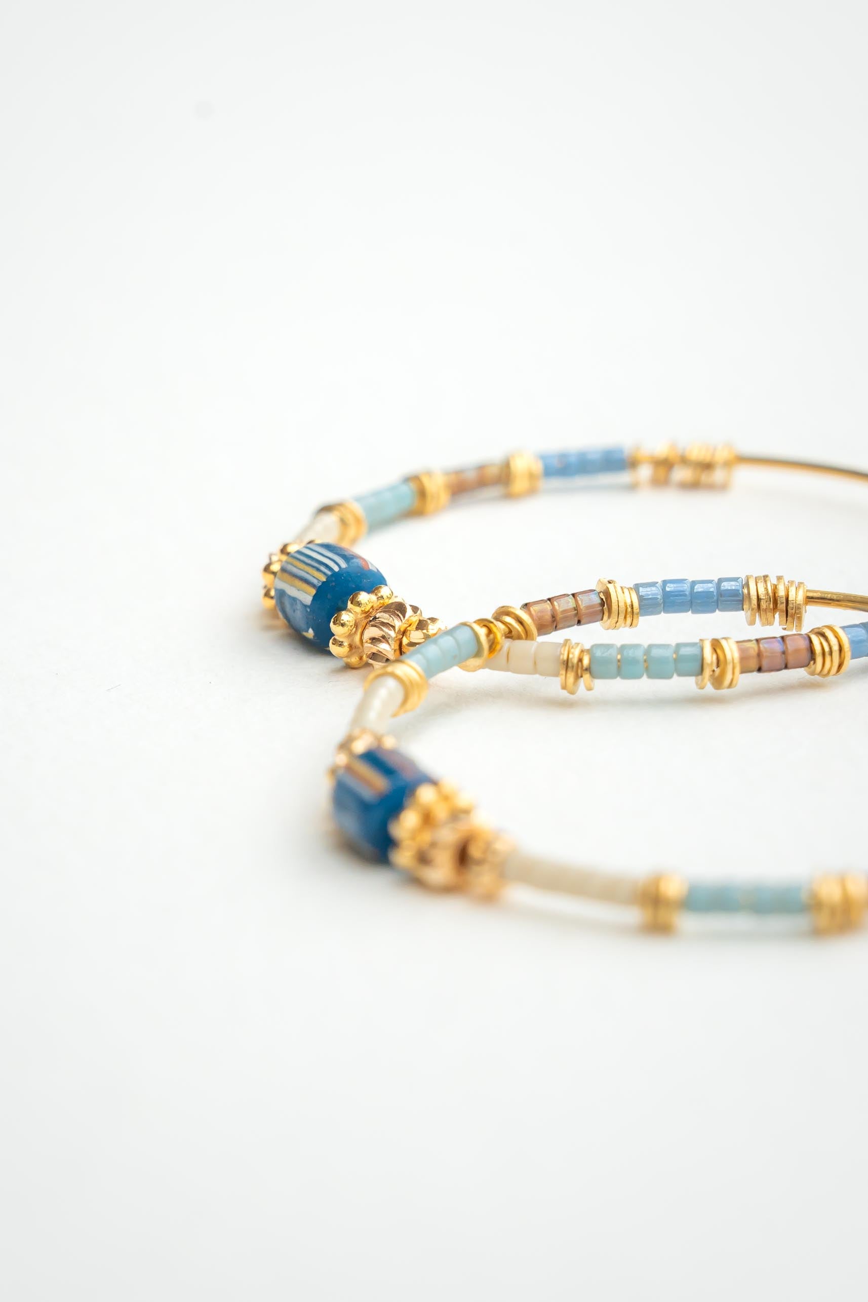 Boucles d’oreilles créoles dorées à l’or fin avec perles africaines bleues rayées rouge et blanc et perles japonaises Byciclou