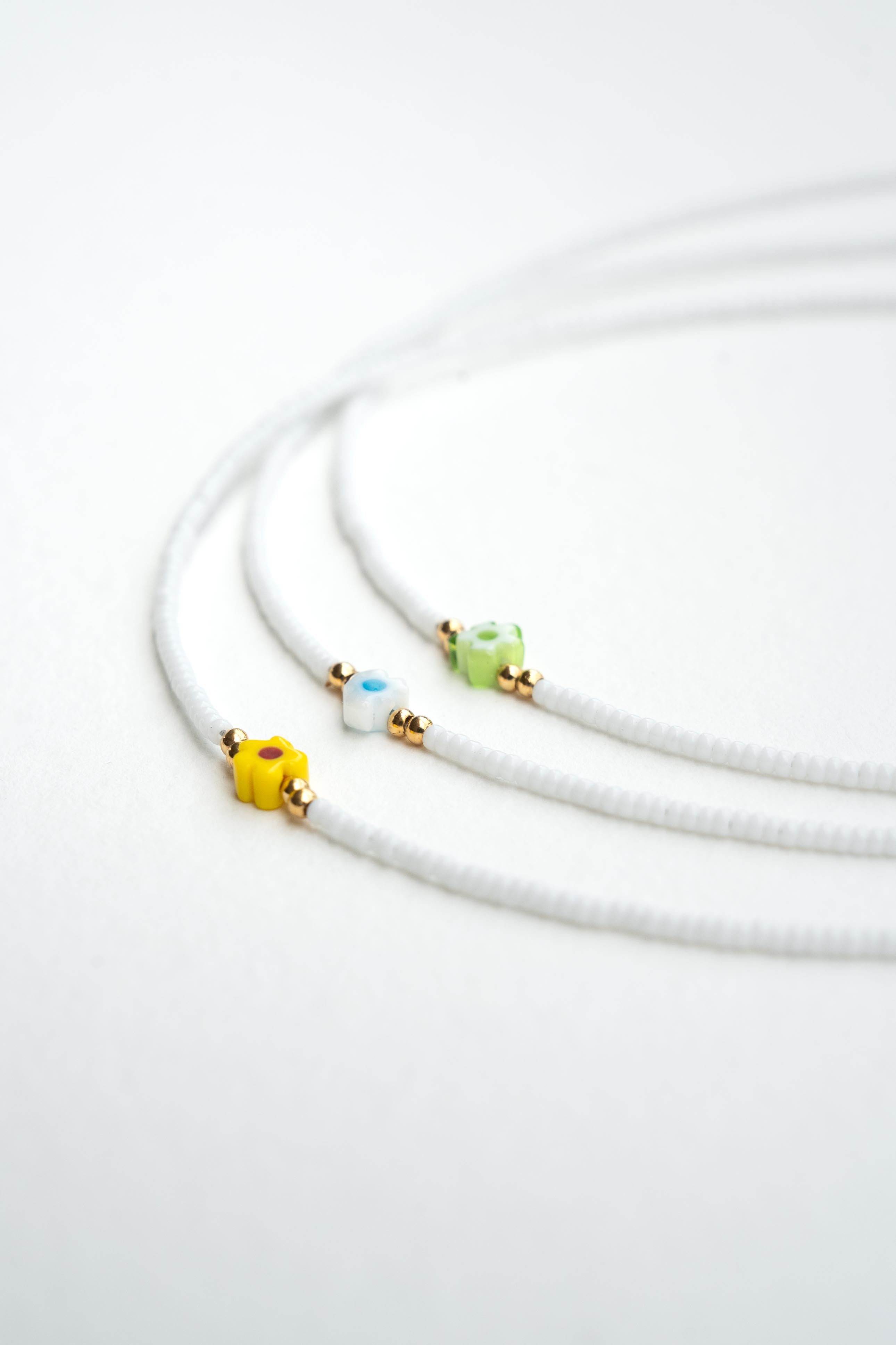 Collier enfant en perles de rocaille blanches avec fleurs jaune, bleu et vert et touches dorées Byciclou